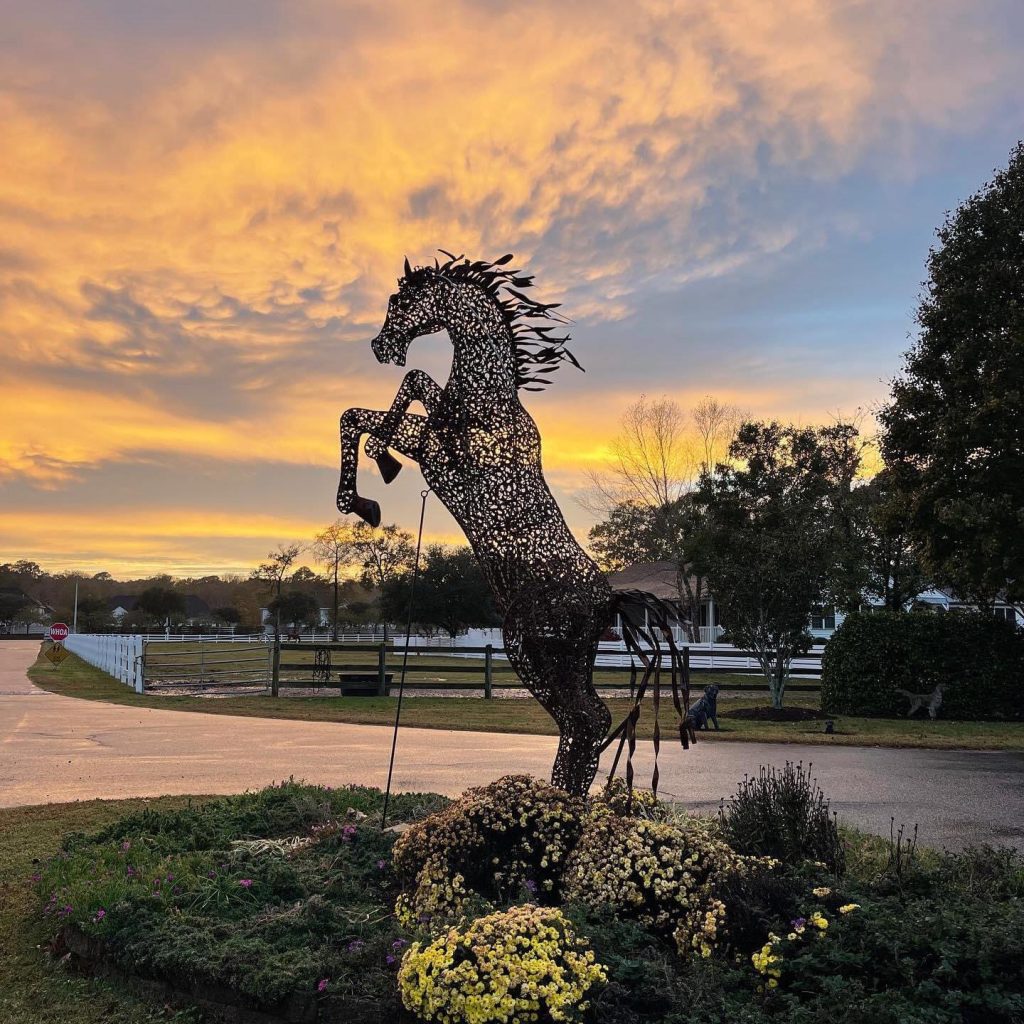 Rearing metal horse sculpture in a landscaped garden at sunset.