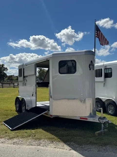 White horse trailer with the side ramp lowered, photographed from a wider angle with an American flag above the hitch.